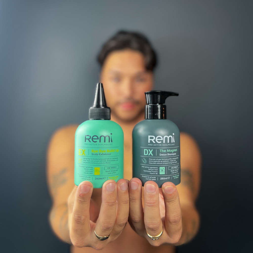 Person holding two Remi hair care products against a dark background