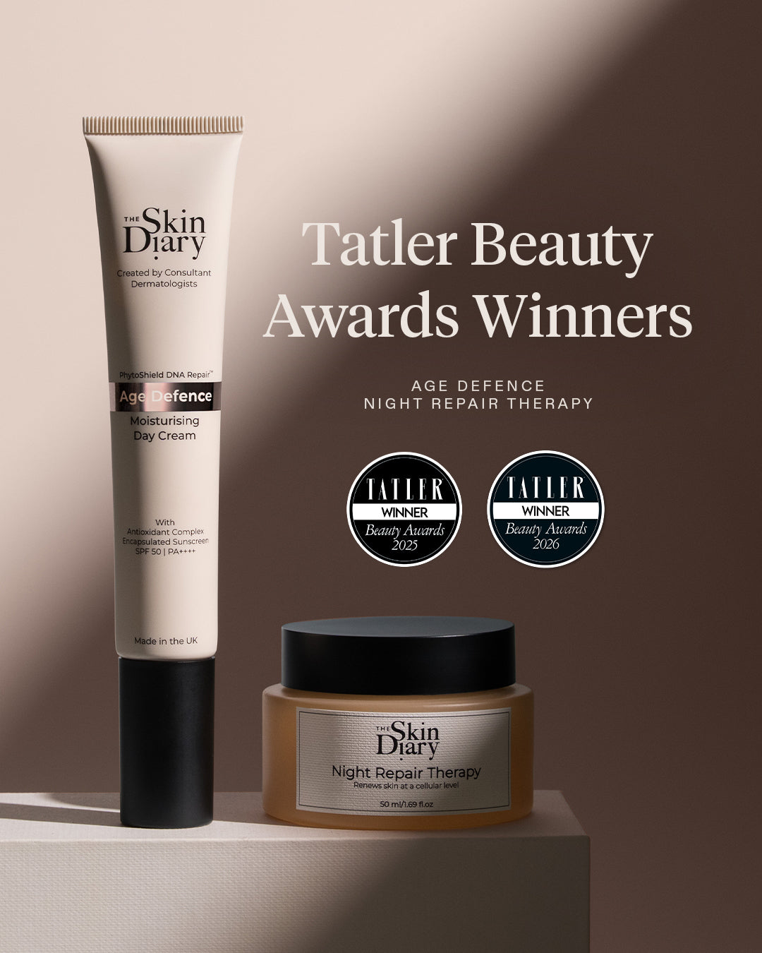 Two skincare products from The Skin Diary are displayed on a pedestal against a warm beige background with dramatic shadows. On the left is a tall white tube labeled Age Defence Moisturising Day Cream, and on the right is a brown jar labeled Night Repair Therapy.
