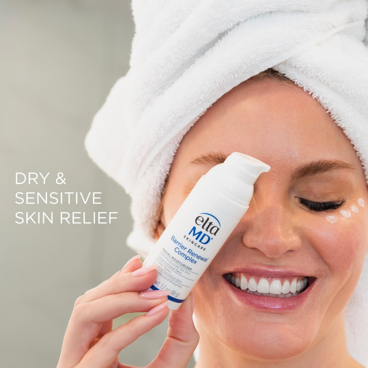 A smiling woman with a white towel wrapped around her head holds a white tube of eta MD Eye Relief Complex near her eye. White dots of cream are visible on her cheek, and the text 'DRY & SENSITIVE SKIN RELIEF' appears on the left against a soft gray background.