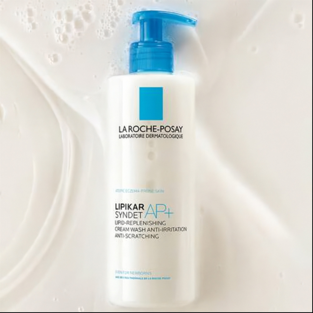 La Roche-Posay Lipikar Syndet AP+ Lip Cream Wash pump bottle in white with a blue pump, set against a background of white lathered soap foam.