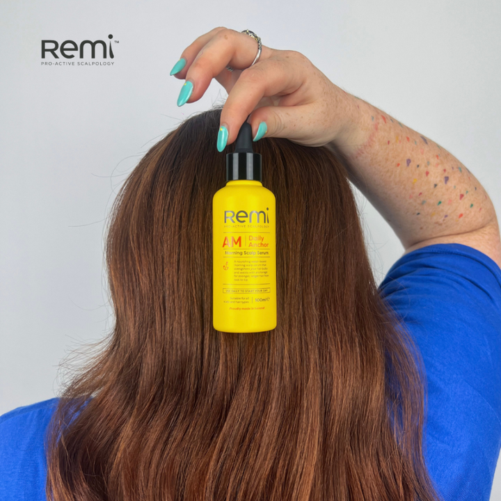 Person using a yellow bottle labeled 'Remi' on their hair against a plain background