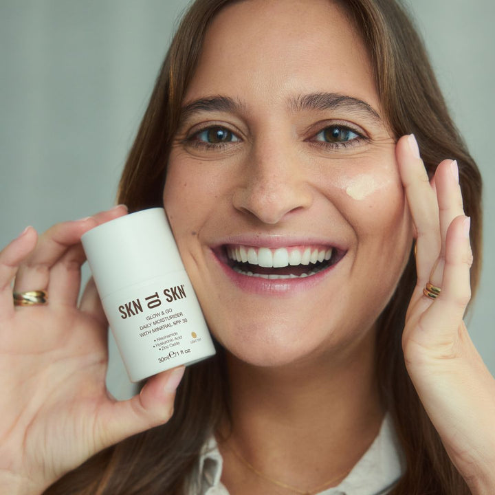 Glow & Go Daily Moisturiser in a white bottle, shown with its light tint blended onto a woman's cheek