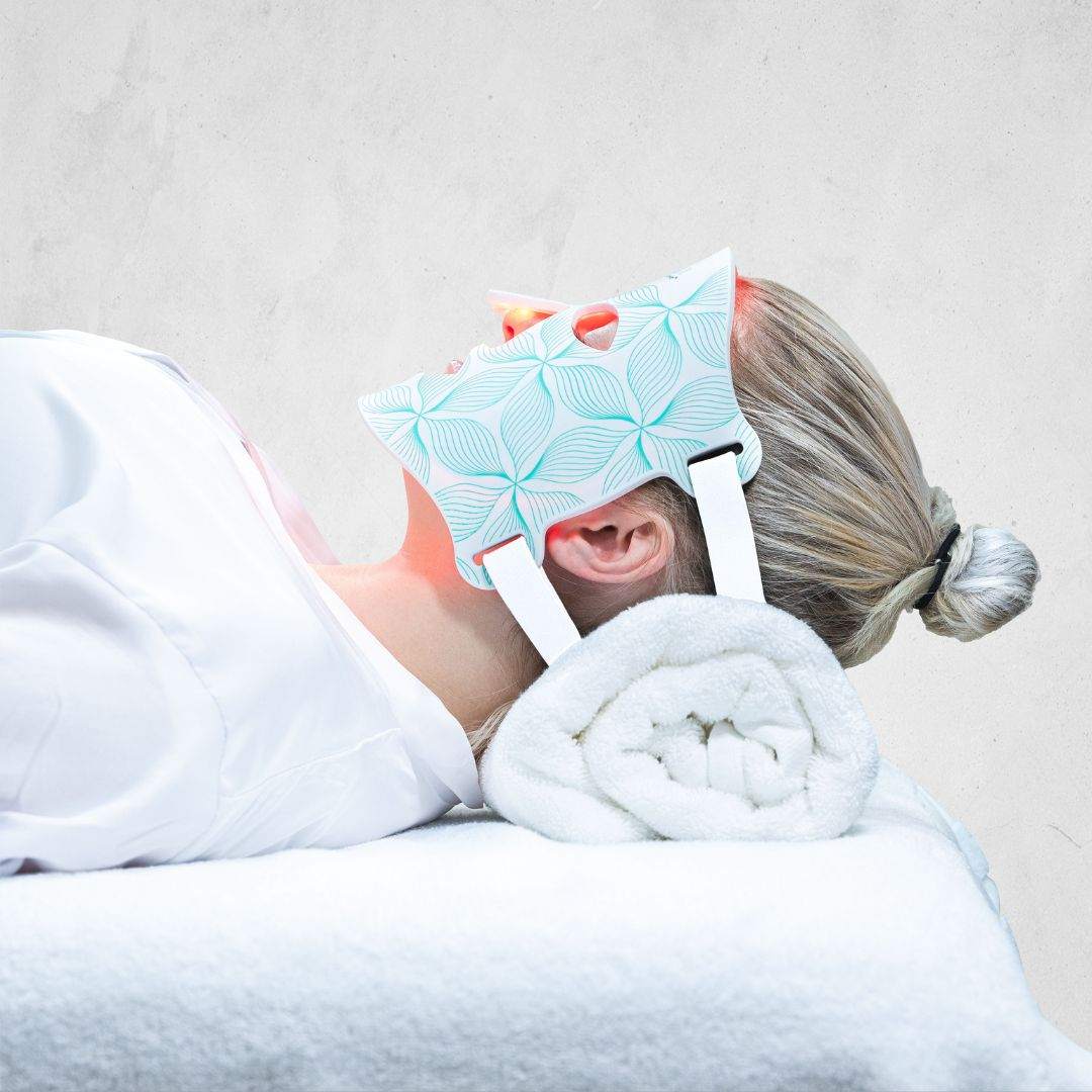 Omnilux Contour Face LED mask with blue patterned cover worn by a reclining person