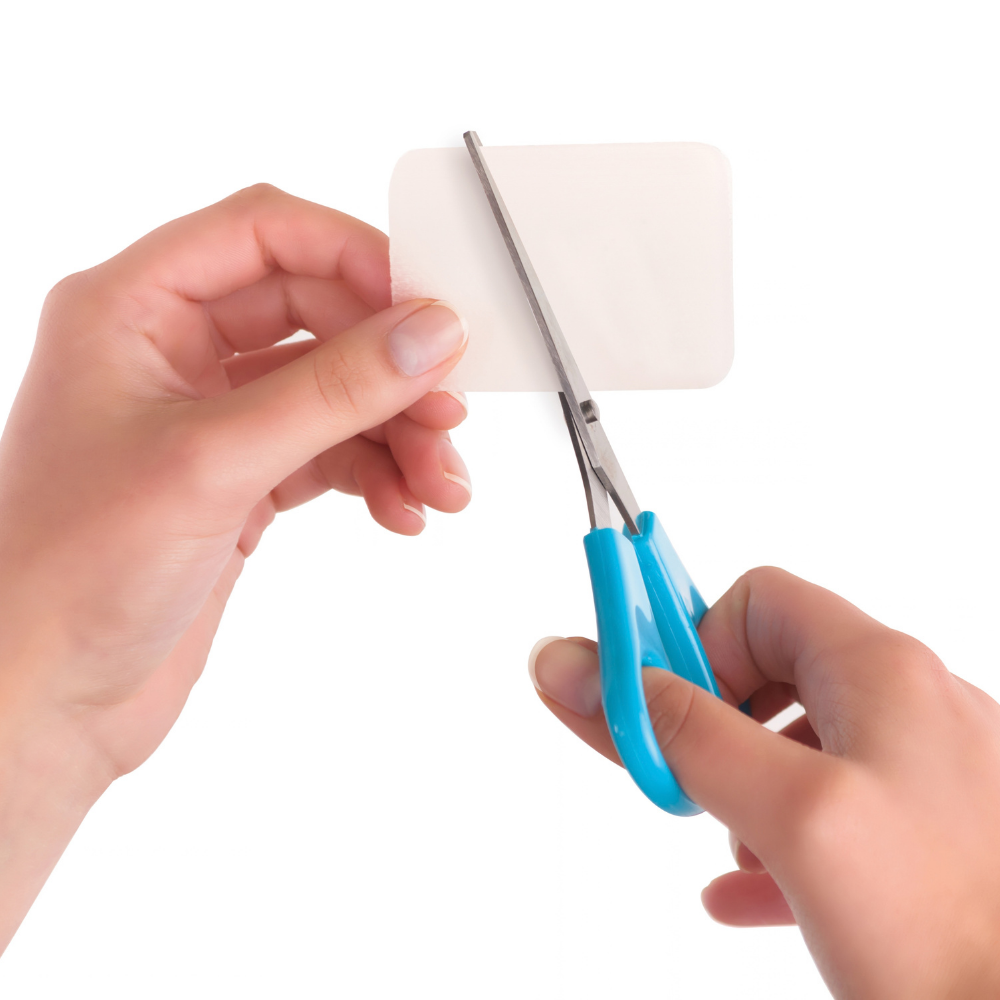 Silicone sheets shown as a thin, flexible translucent sheet being trimmed with blue-handled scissors