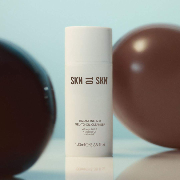 Skn to Skn Balancing Act Gel-To-Oil Cleanser in a white cylindrical pump bottle with brown logo