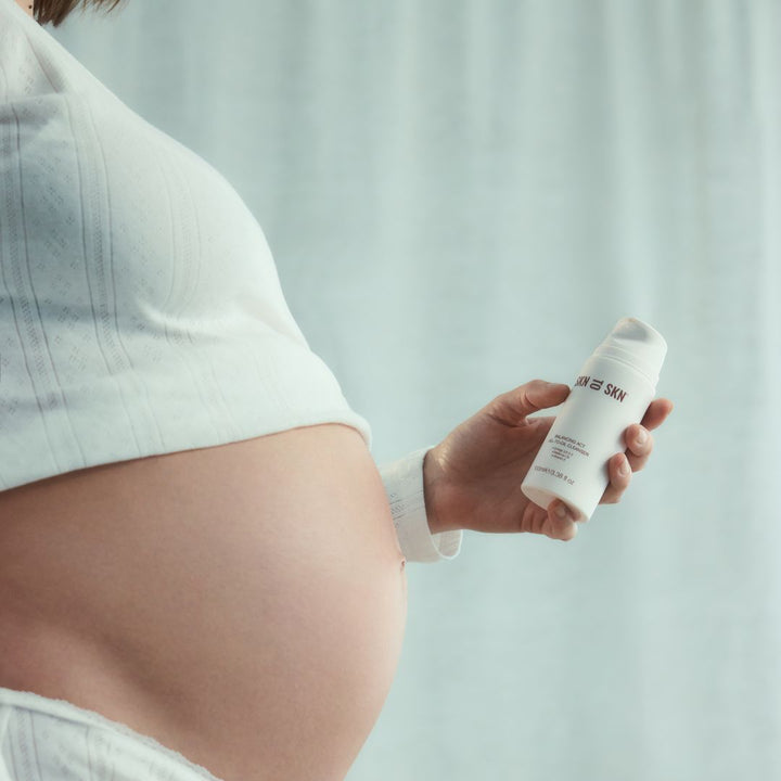 Skn to Skn Balancing Act Gel-To-Oil Cleanser white cylindrical bottle held beside a pregnant belly